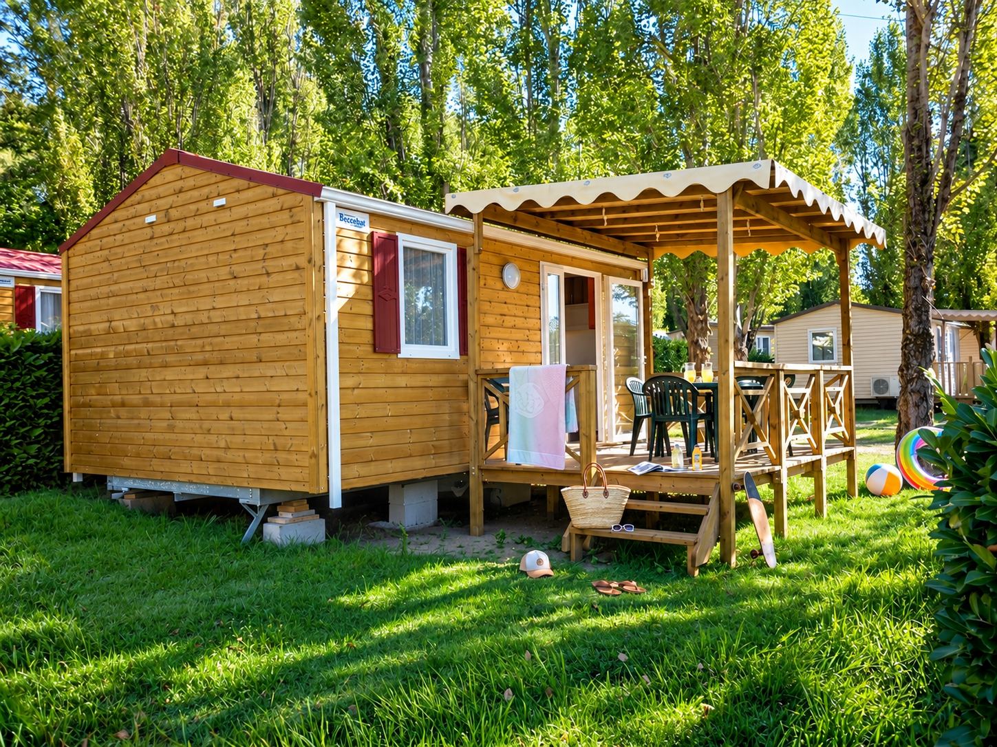 Mobil-home en bois avec terrasse au camping Fleur de Camargue : terrasse couverte avec table et chaises, sur une pelouse ombragée.
