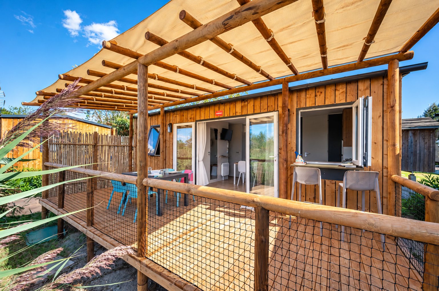 Mobil-home en bois avec terrasse au camping Fleur de Camargue : terrasse sous pergola devant un comptoir bar extérieur et ses tabourets.
