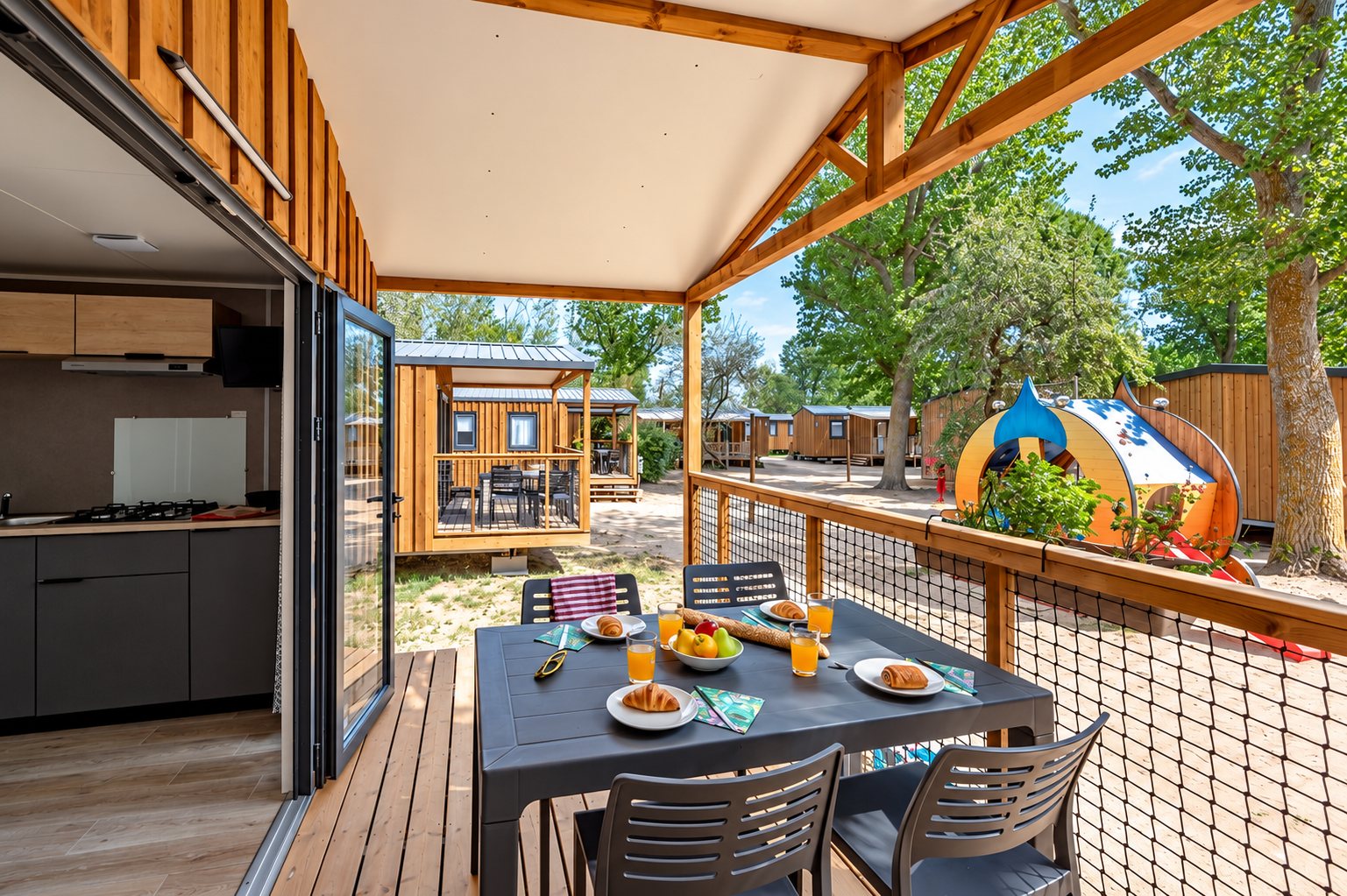 Mobil-home en bois avec terrasse au camping Fleur de Camargue : table de petit-déjeuner dressée sur la terrasse couverte, face aux autres hébergements.